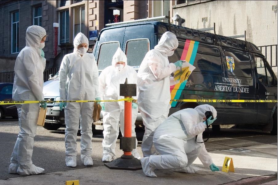 Criminology students dressed in white suites investigating a mock crime scene. 