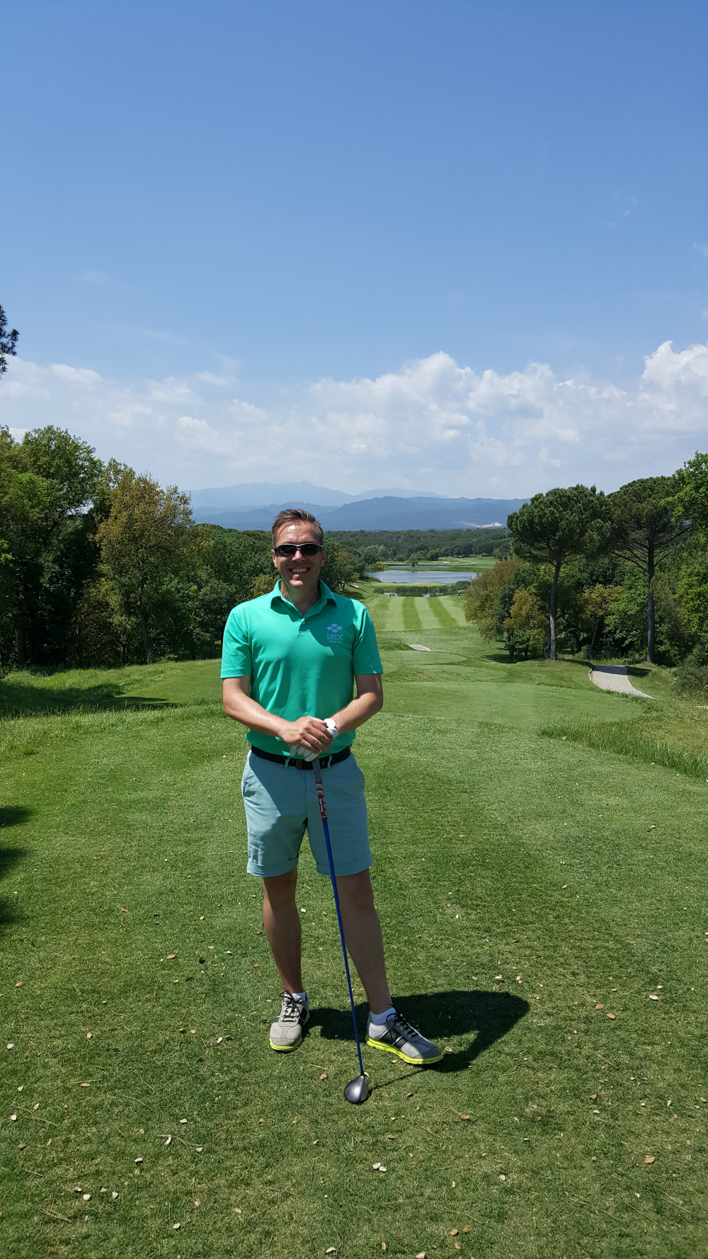Fraser on a golf course with mountains in the background and a golf club in his hands
