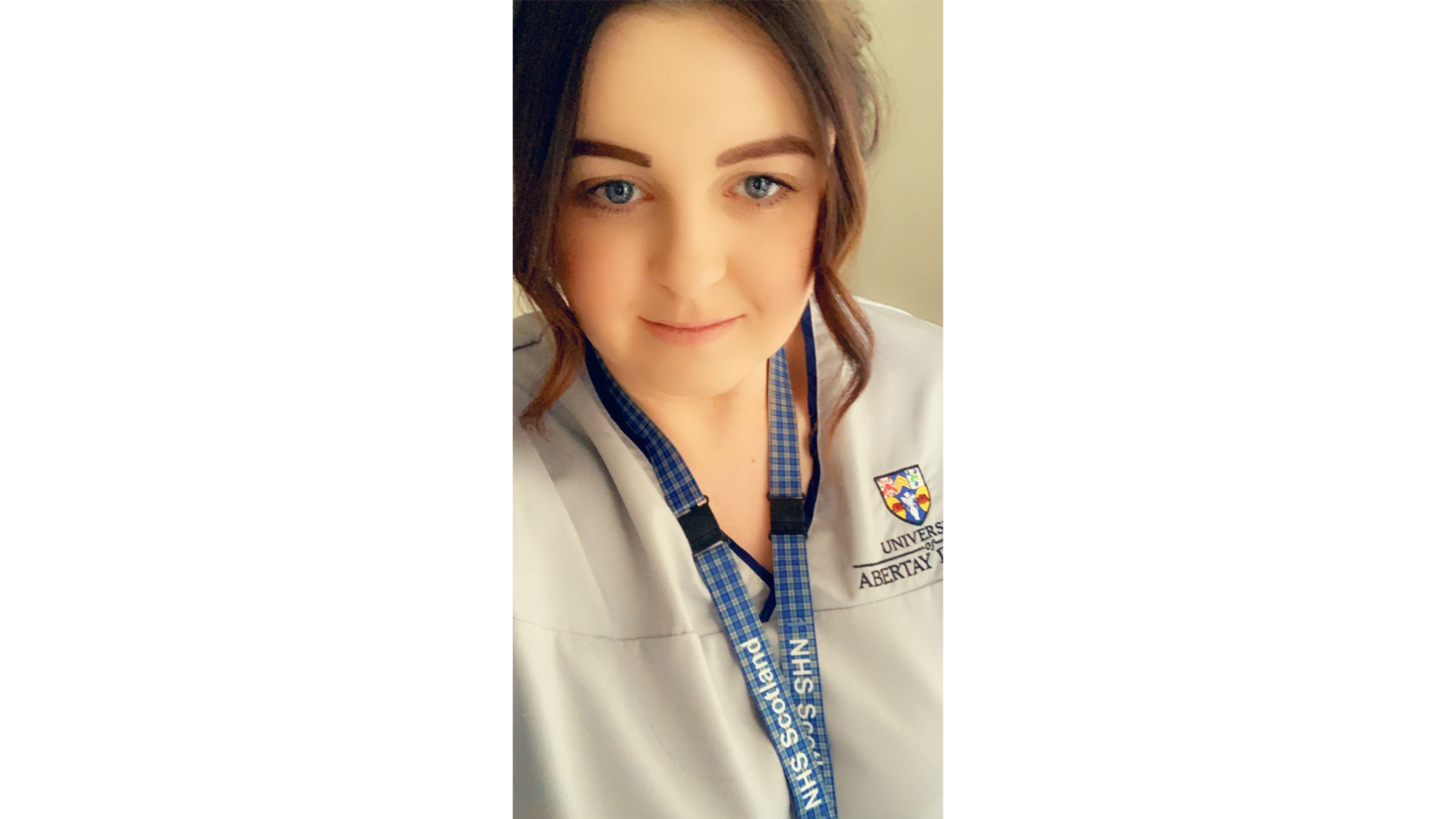 A selfie of Caroline Ford, in a nurses uniform with an Abertay University logo on her right. Caroline is also wearing an NHS Scotland lanyard arount their neck.