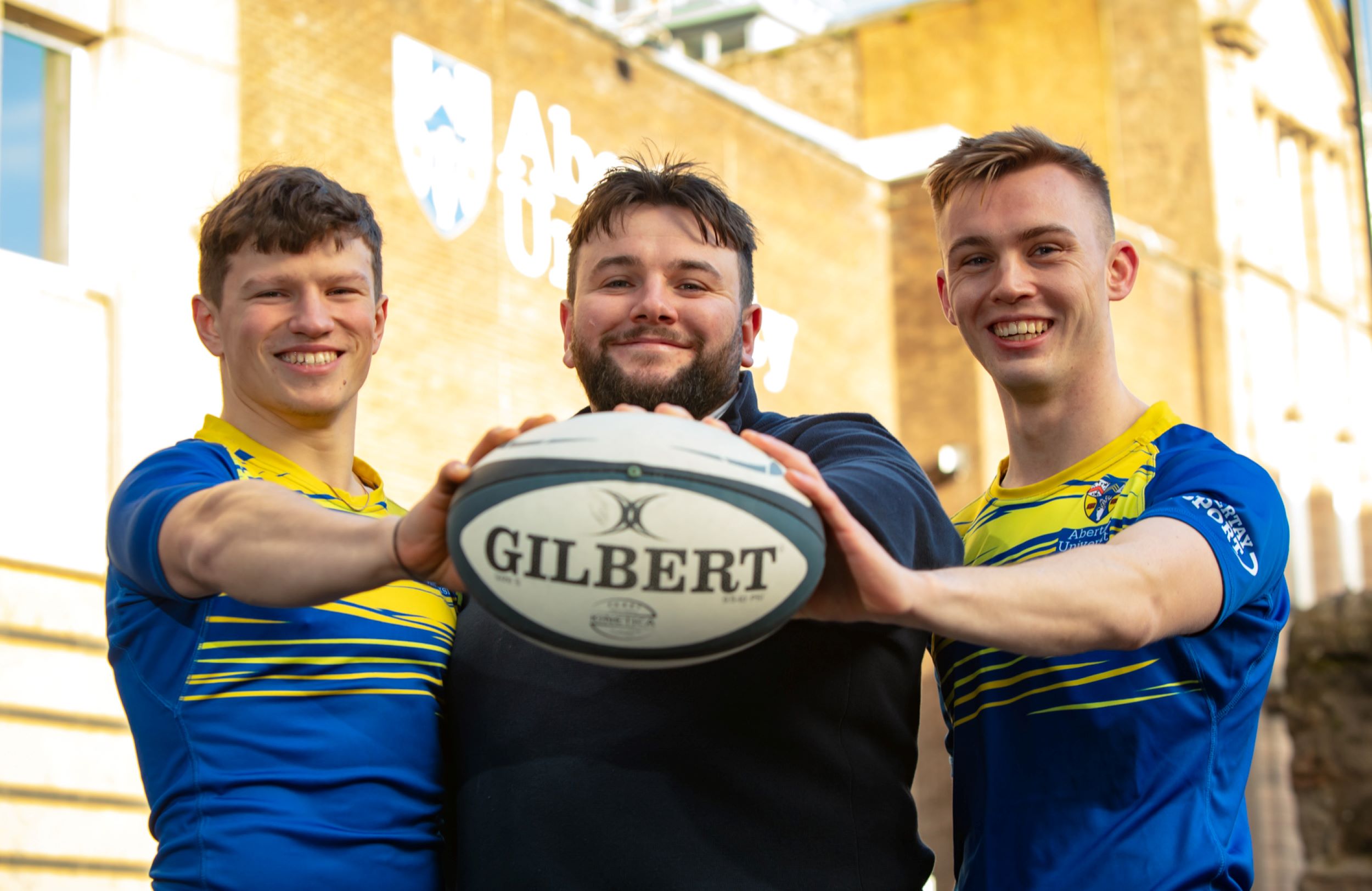 3 rugby club members holding ball towards viewer