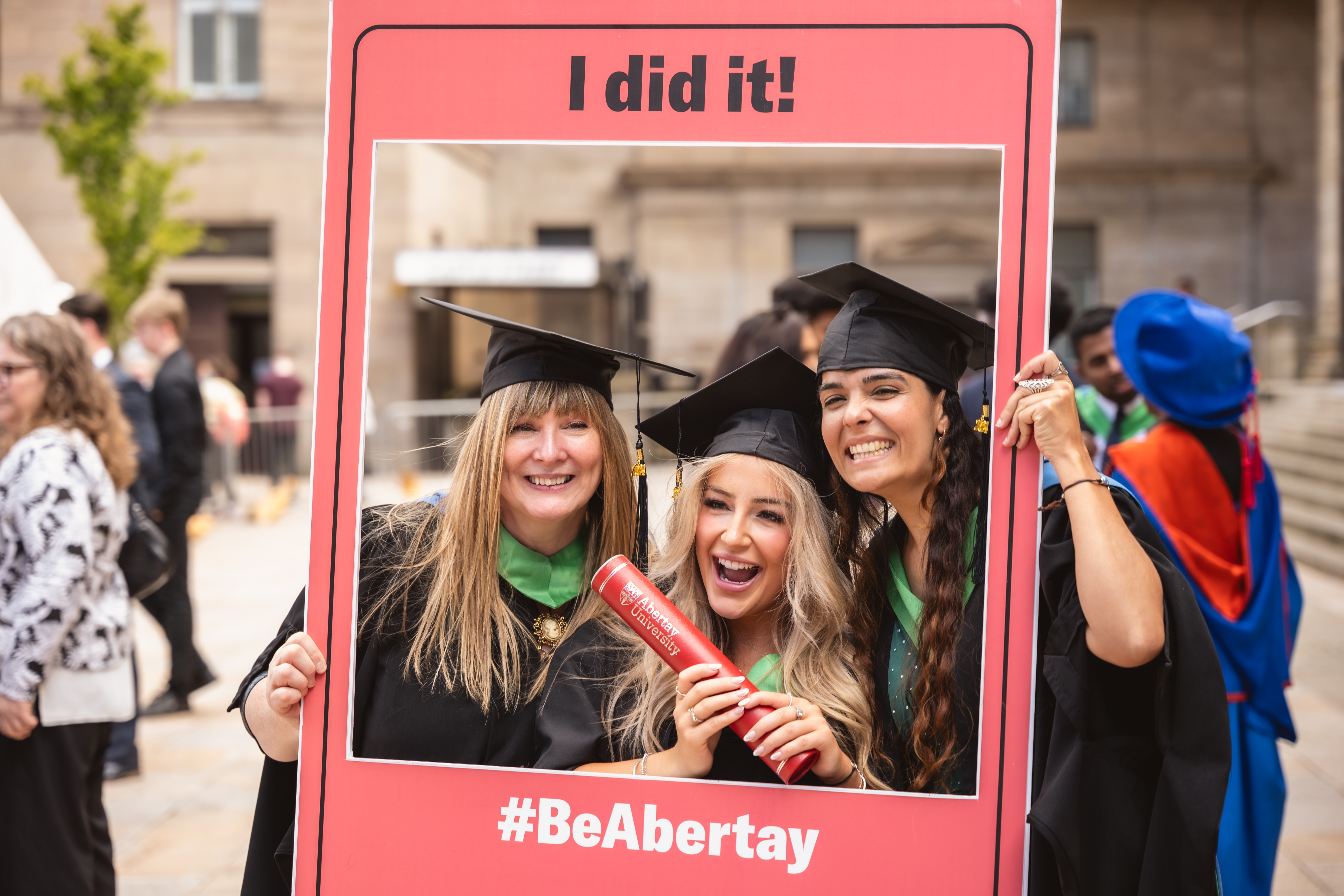 Students in graduation robes posing within a large red photo frame