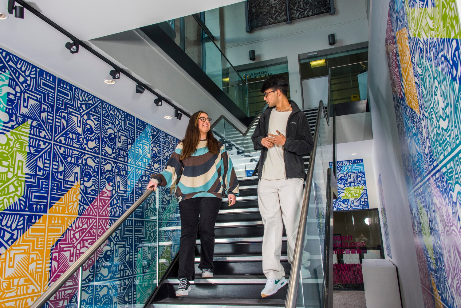 Two students chatting and descending the stairs at Abertay 